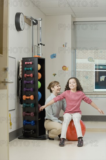 Physical therapist helping girl on exercise ball