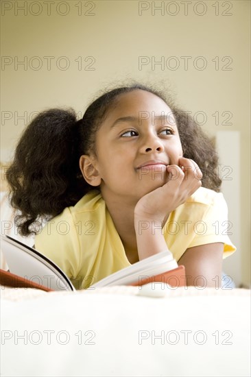 African American girl reading book in bed