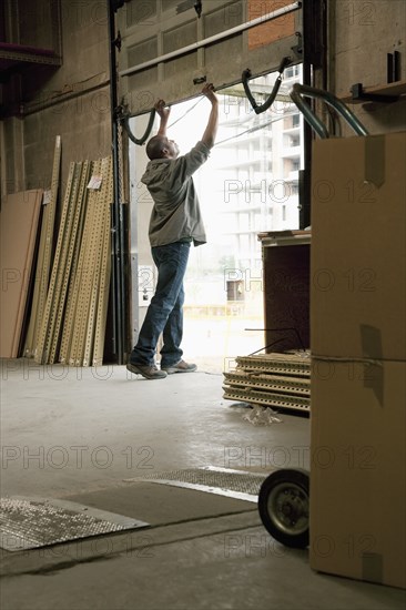 Black man closing loading dock door in warehouse