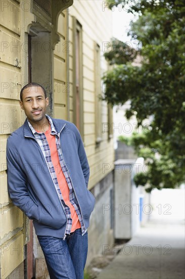 African American man leaning against side of building