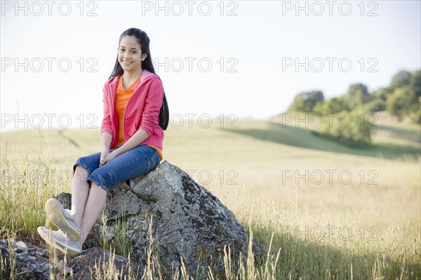 Hispanic girl sitting on rock in field