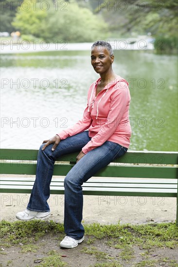 African American woman sitting on park bench near lake