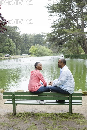 African American couple sitting on bench near lake