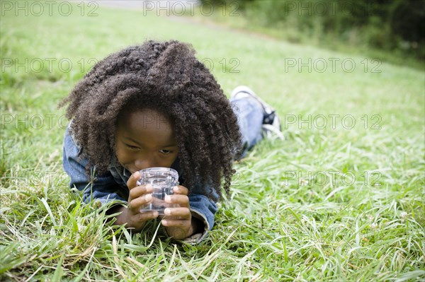 African American boy laying in grass and looking in jar