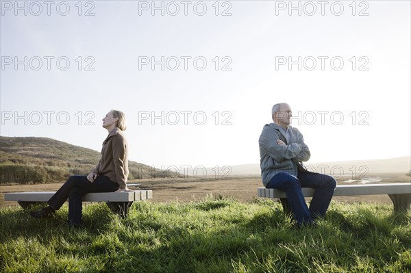 Caucasian sitting back to back on benches at beach