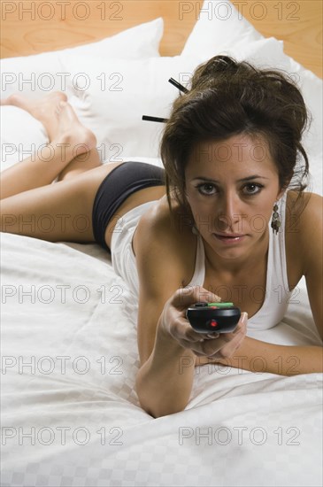 Hispanic woman laying on bed with remote control