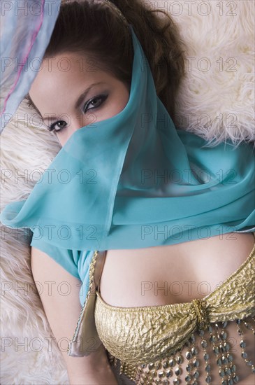 Woman wearing belly dancing outfit with veil and laying down