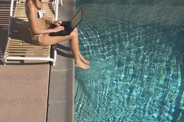 Woman typing on laptop with feet in swimming pool