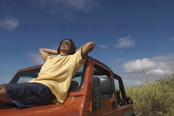 Asian man reclining on hood of jeep