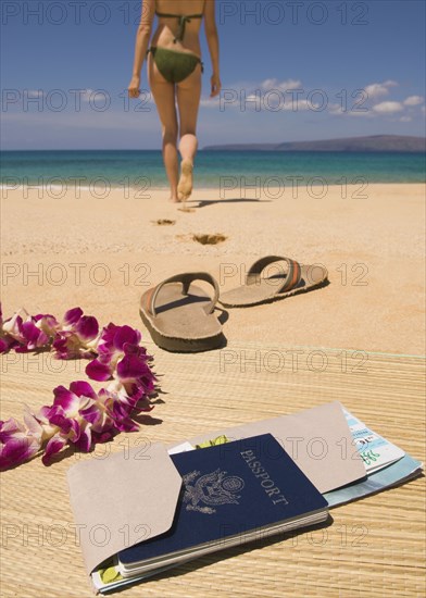 Woman walking away from passport and sandals on beach