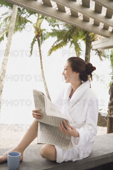 Asian woman in bathrobe reading newspaper