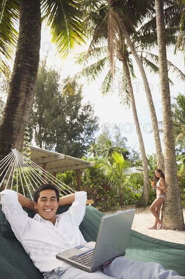 Asian man with laptop in hammock