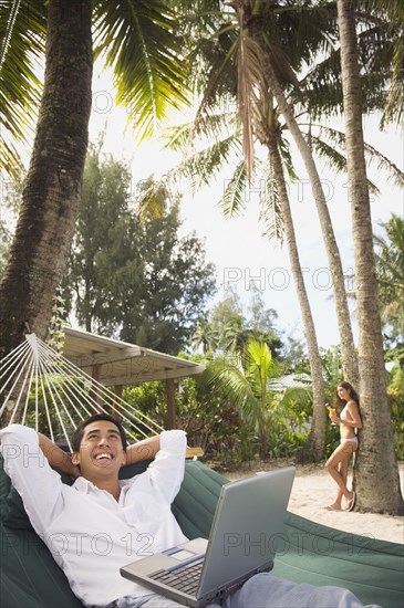 Asian man with laptop in hammock