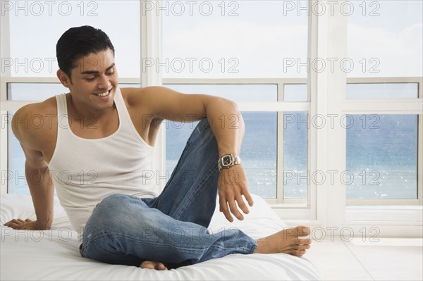 Hispanic man sitting on bed