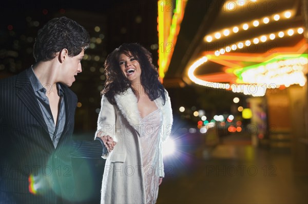 Multi-ethnic couple holding hands and laughing outside nightclub