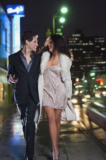 Multi-ethnic couple in formal attire walking down sidewalk