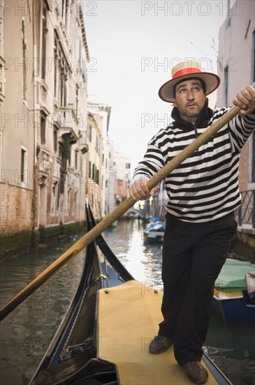 Italian gondolier rowing gondola through canal