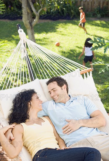 Couple in hammock with children playing in background