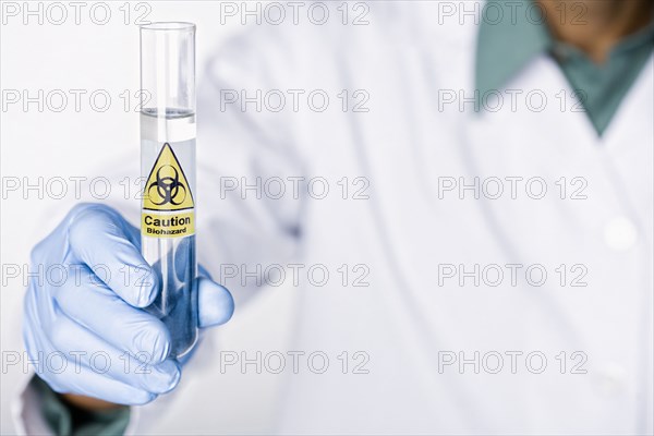 Hispanic scientist holding test tube with caution sticker full of water