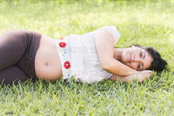 Mixed race pregnant woman laying in grass