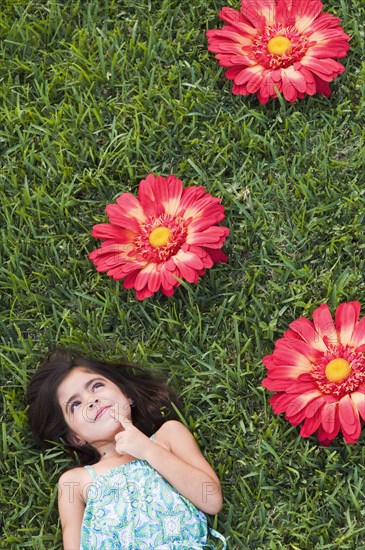 Mixed race girl laying in grass next to large flowers