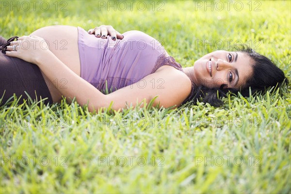 Mixed race pregnant woman laying in grass