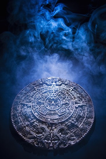 Aztec calendar stone carving surrounded by smoke