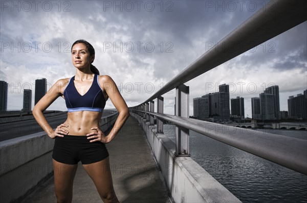 Hispanic woman in sportswear standing near urban waterfront