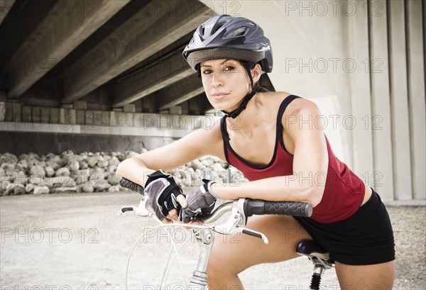 Hispanic woman sitting on bicycle in urban area