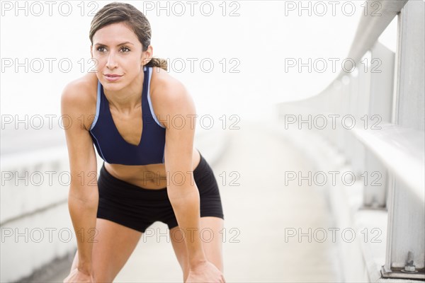 Hispanic woman in sportswear resting on sidewalk