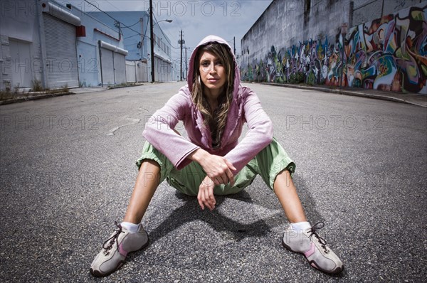 Hispanic woman sitting in alley with graffiti