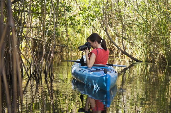 Hispanic woman in kayak photographing everglades