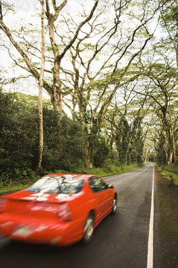 Red car driving down country lane