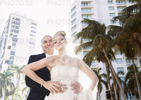 Hispanic bride in groom hugging outdoors