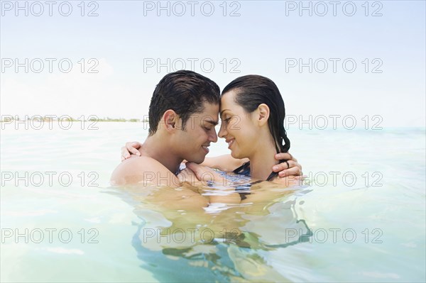 Hispanic couple hugging in water