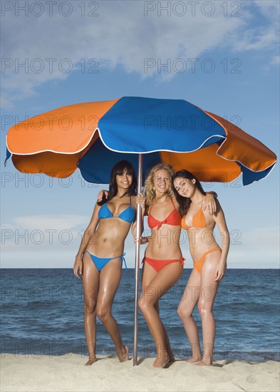 Women in bikinis under beach umbrella