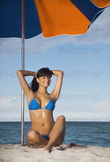 Hispanic woman in bikini under beach umbrella