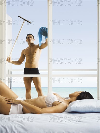 Woman in bed watching boyfriend wash windows