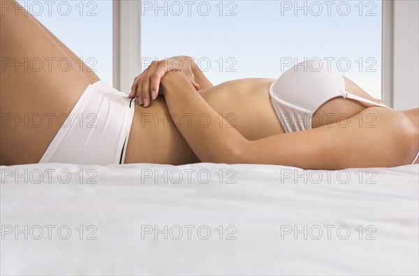 Hispanic woman in bra and underwear laying on bed