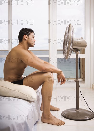 Hispanic man sitting in front of fan