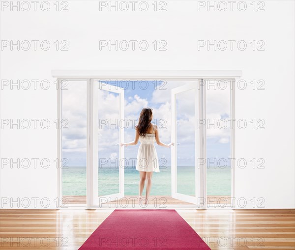 Hispanic woman opening French doors to ocean view