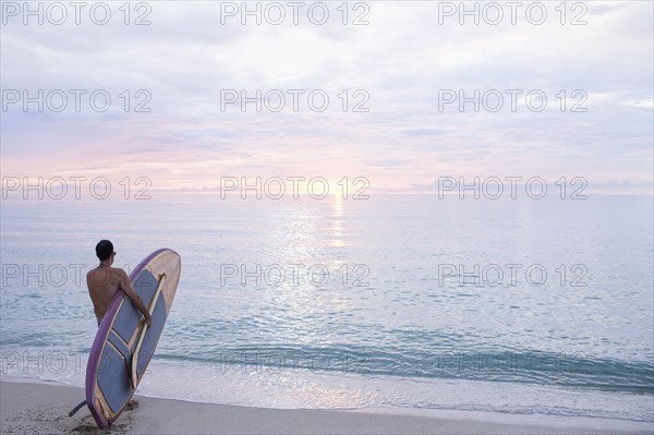 Caucasian surfer holding paddleboard on beach