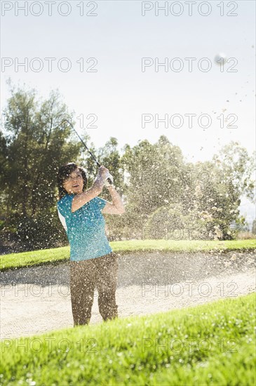 Korean woman hitting ball in sand trap on golf course