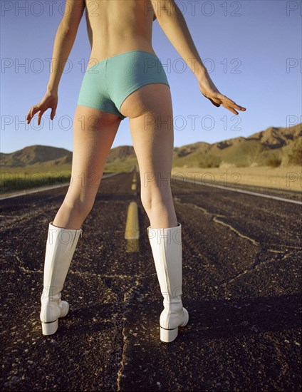 Caucasian woman wearing boots and panties standing in middle of road