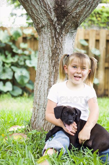 Caucasian girl leaning on tree hugging dog