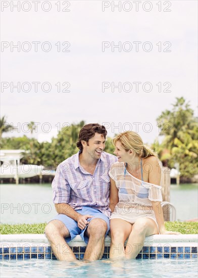 Caucasian couple sitting at the edge of swimming pool