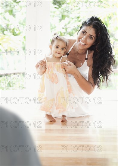 Mixed Race mother kneeling on floor helping baby daughter walking