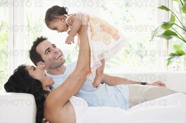 Mixed Race mother and father playing on sofa with baby daughter