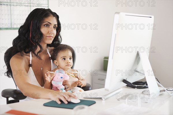 Mixed Race mother using computer and holding baby daughter