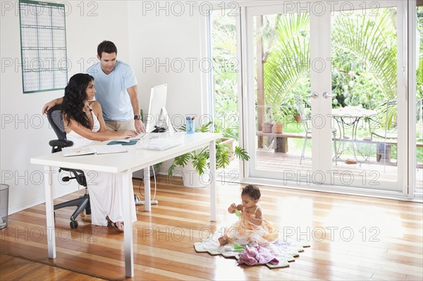 Mixed Race mother and father using computer and watching baby daughter